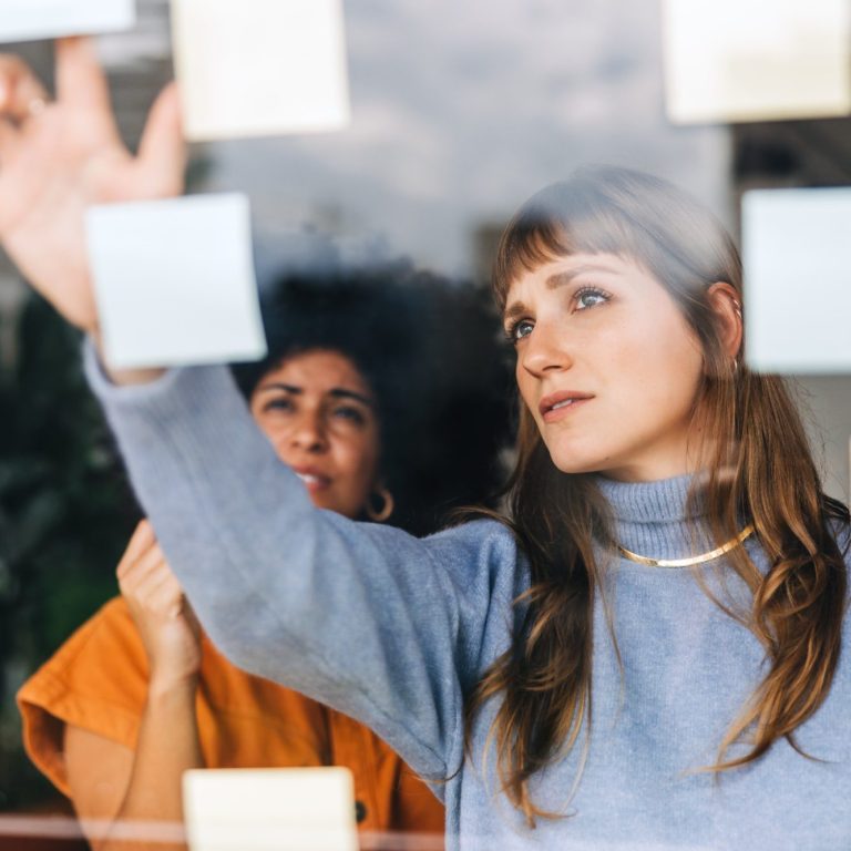 Zwei Frauen diskutieren und kleben bunte Notizen an ein Fenster.